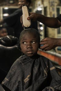 A young boy gets a haircut in an urban barbershop, showcasing grooming and childhood experiences.