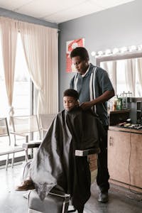 A young boy receives a haircut from a barber in a modern salon setting, showcasing a typical salon experience.