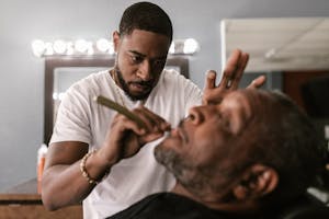 Barber providing a straight razor shave to a customer in a barbershop setting.