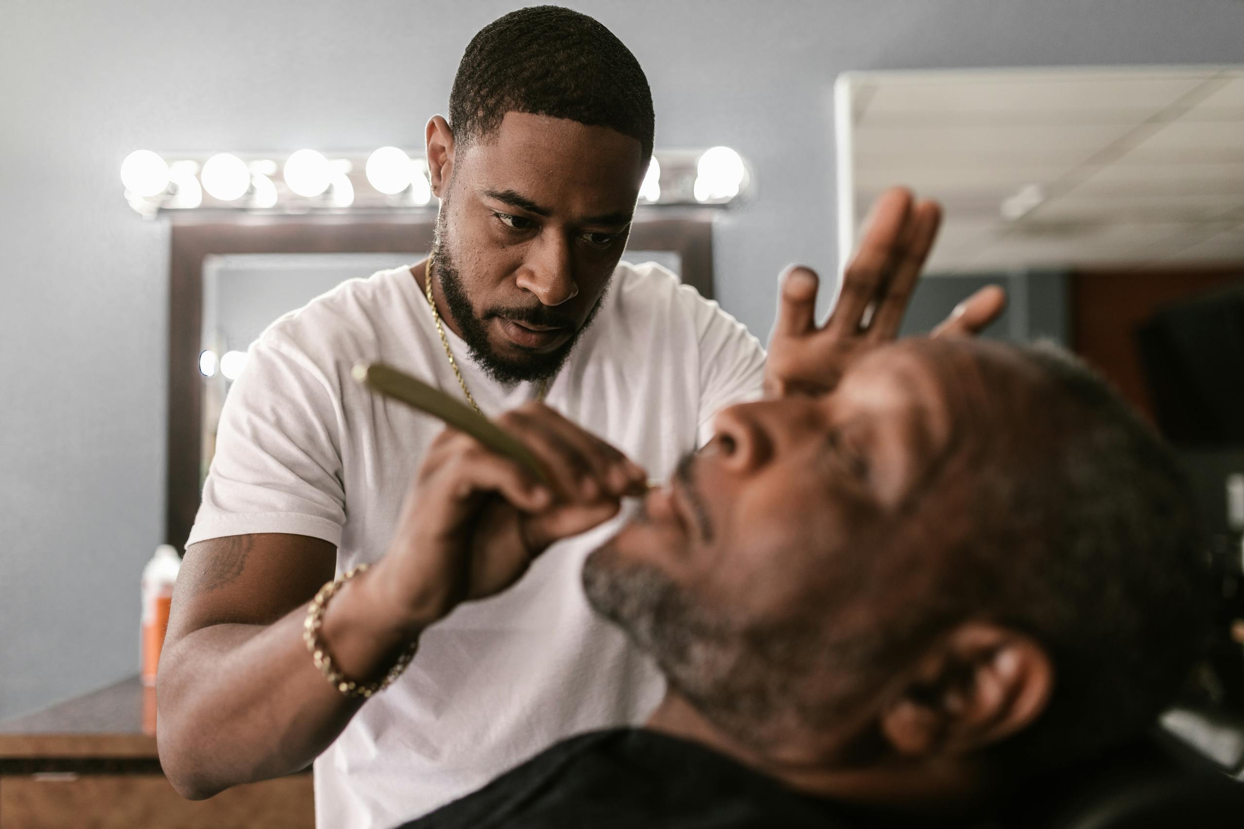 Barber providing a straight razor shave to a customer in a barbershop setting. Barber providing a straight razor shave to a customer in a barbershop setting.
