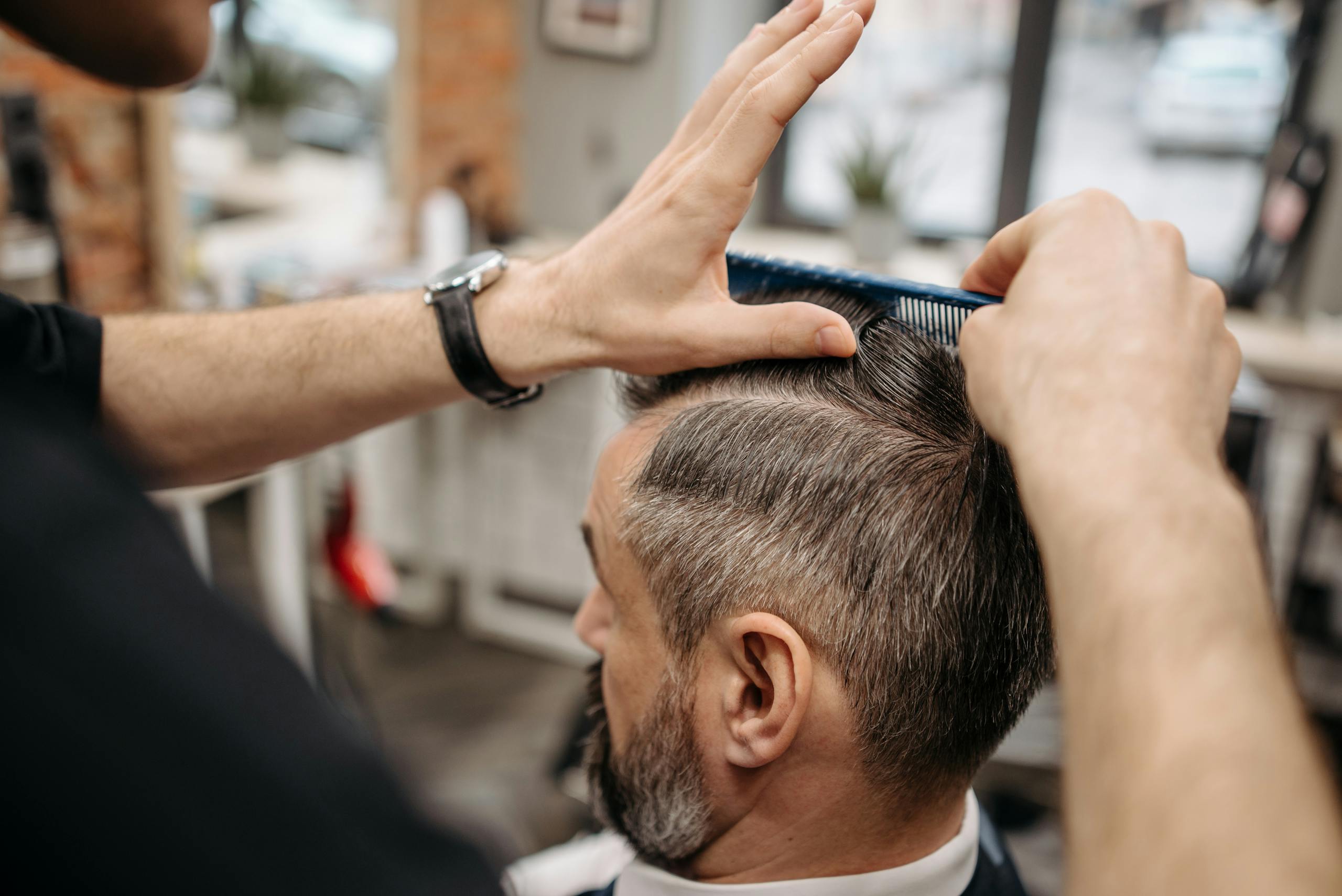 Close-up of a barber styling a customer's hair in a modern barbershop setting. Close-up of a barber styling a customer's hair in a modern barbershop setting.